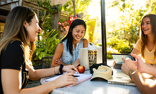 three UCF students sit around an outside table with notebooks and pens