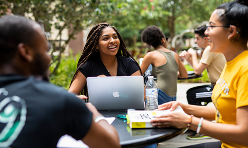 UCF students sit around an outside table wit their laptops and notebooks