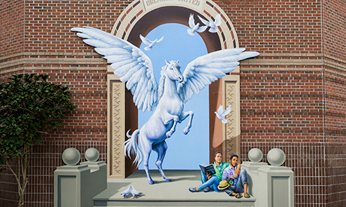 Pegasus mural with birds flying above it and students sitting below it painted on a UCF brick building