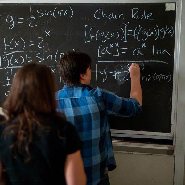 student writing in chalk on a black board