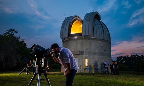 students looks through a telescope in front of the UCF observatory