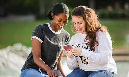 Two students smiling looking at a phone
